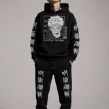 A man modeling a black Jujutsu Kaisen hoodie and matching sweatpants set. The hoodie features a large white graphic of the character Satoru Gojo on the chest, with white kanji and text printed down both sleeves.